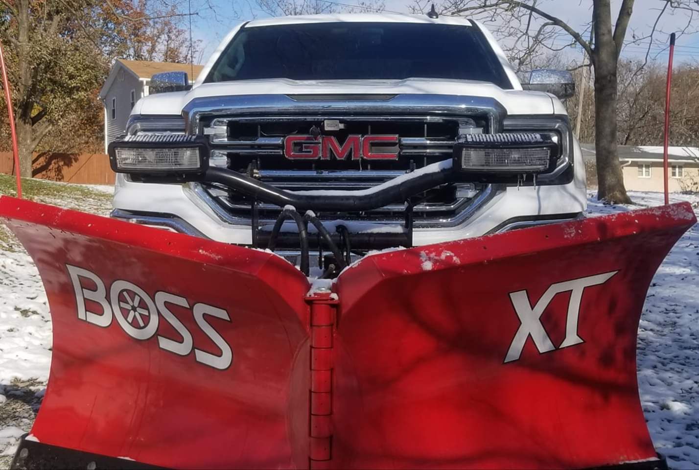 A pickup truck fitted with a red V-plough, standing on a light covering of snow.